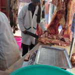 Picture of butcher's shop, there is meat hanging down and a man in a white coat is cutting meat