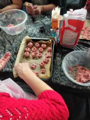 Image of someone's hands placing pink cookies into a baking tin, lined with baking paper